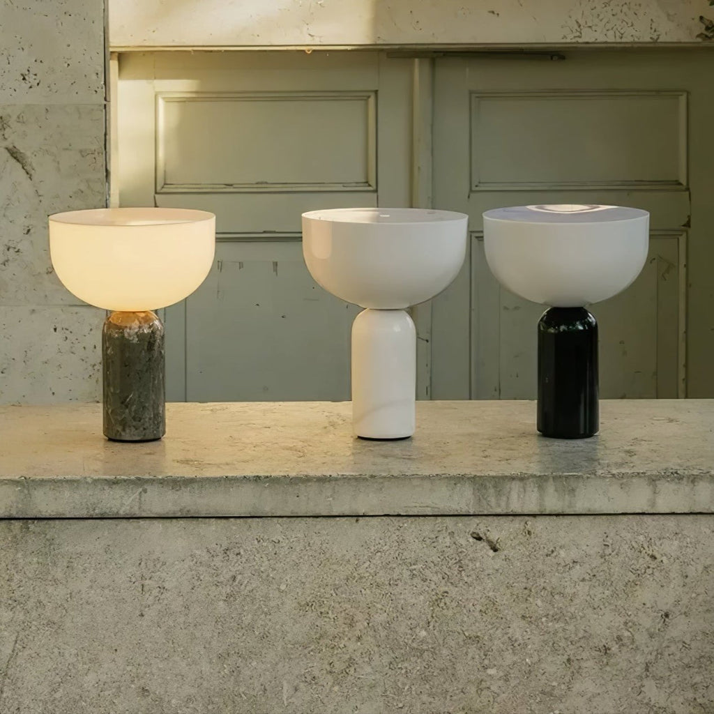 Three Clérachic sphere lamps in grey, white and black marble stand together on a concrete ledge outdoors.