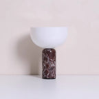 Clérachic's sphere table lamp in dark red marble, photographed against a warm beige studio backdrop.