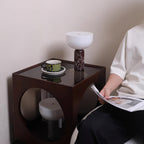 Clérachic's dark red marble lamp lit on a small cube side table while someone reads in a nearby armchair.