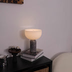 Clérachic's grey marble sphere lamp lit beside a stack of books and small chrome ornaments on a dark table.