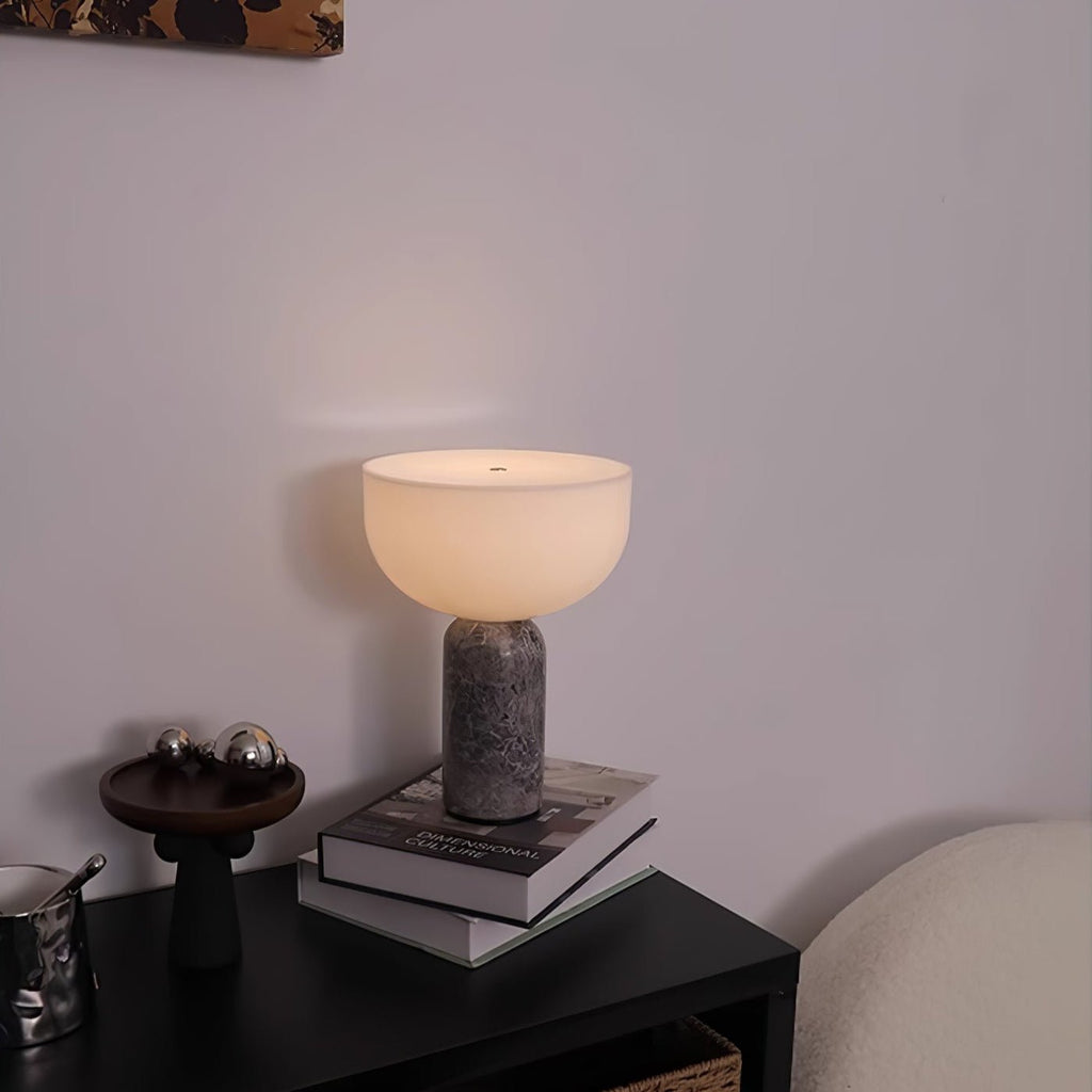 The same grey marble Clérachic lamp seen from a slightly different angle, lit beside books on a dark table.