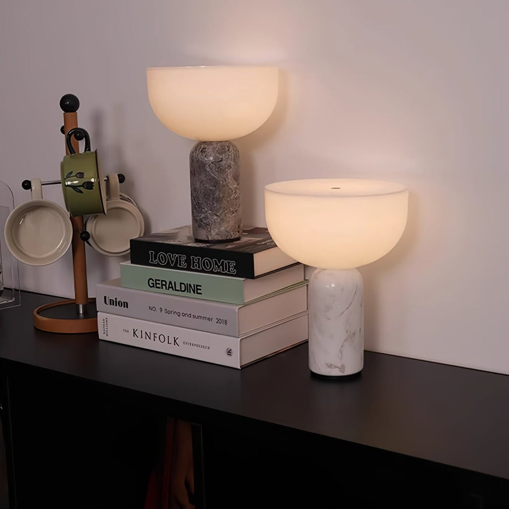 Two Clérachic sphere lamps, one grey marble and one white, stand together on a stack of books on a dark shelf.