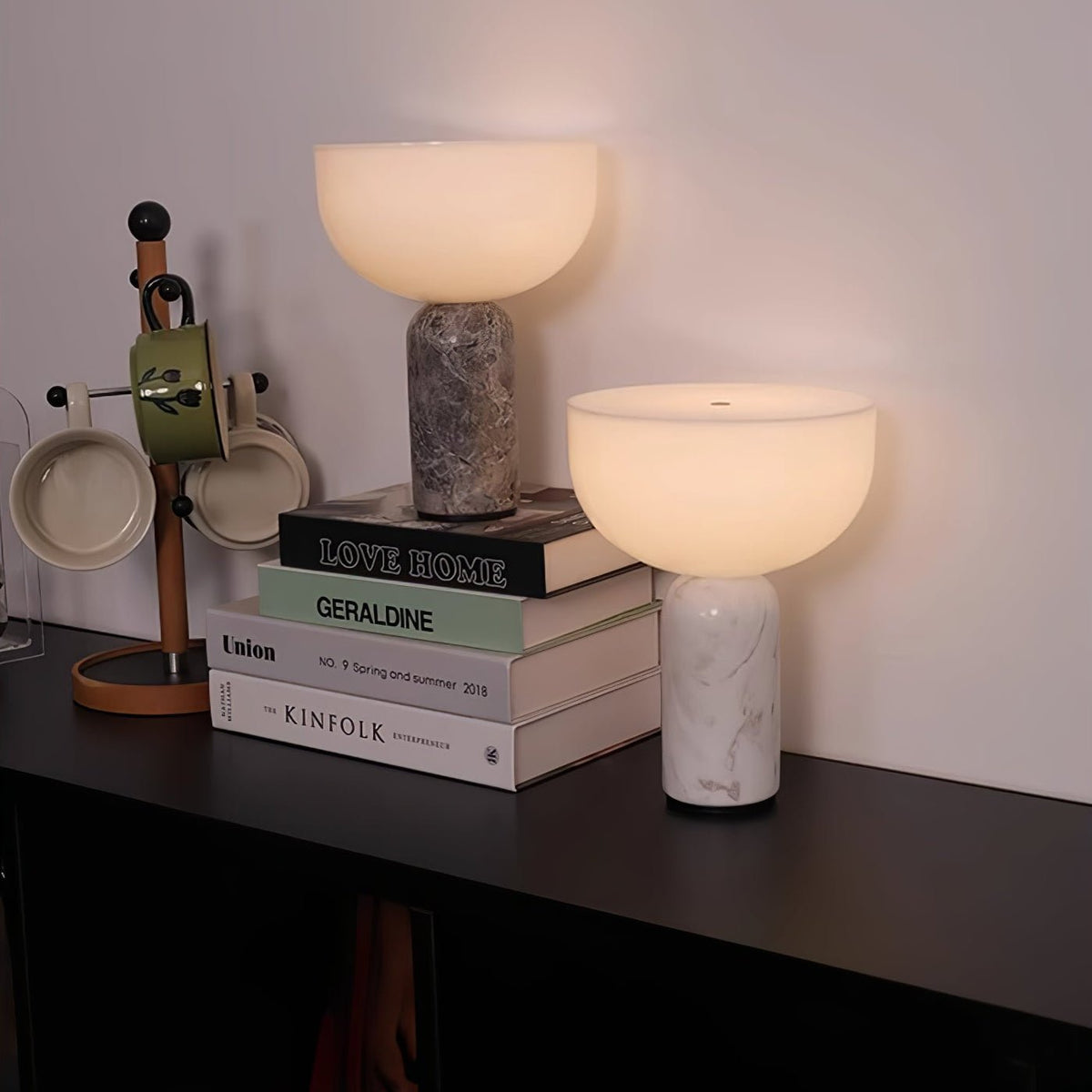 Two Clérachic sphere lamps, one grey marble and one white, stand together on a stack of books on a dark shelf.