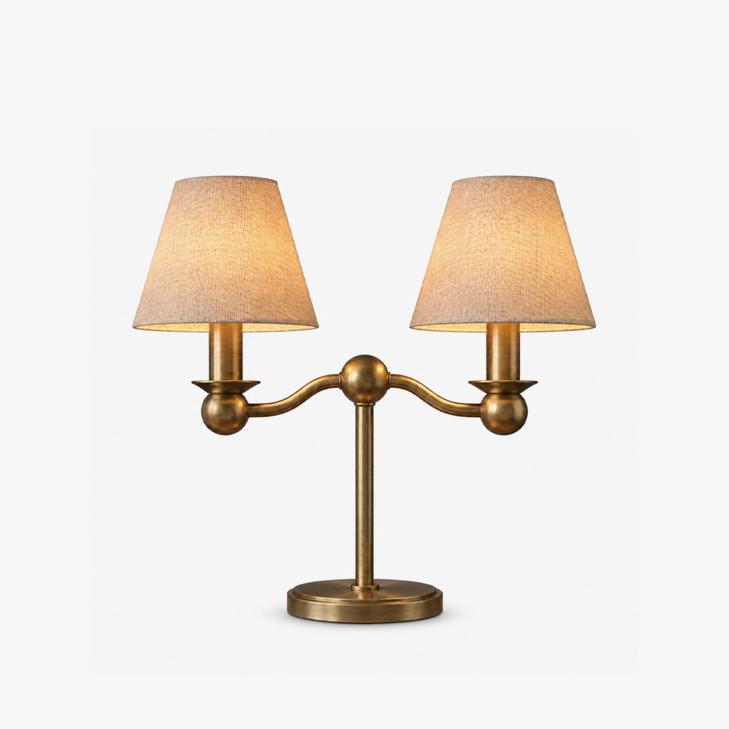 A brushed brass Clérachic table lamp with twin fabric drum shades on ball-jointed arms, photographed unlit on a plain background.