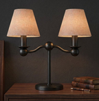 In matte black, this Clérachic table lamp pairs two fabric drum shades on a dark wood nightstand beside stacked books.