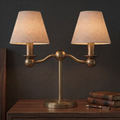 Close on its ball-jointed arms, this brushed brass Clérachic table lamp glows beside a stack of leather-bound books.