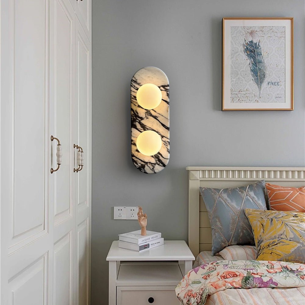 Clérachic marble wall light lit above a white nightstand with books, beside a framed print and floral bedding.