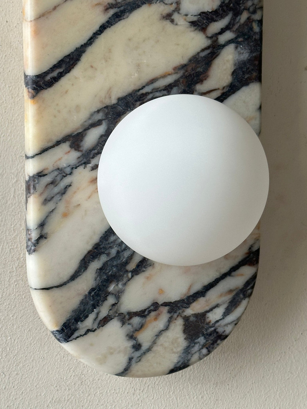 Clérachic marble wall light in close-up, showing the lower globe and the rounded foot of the marble plate.