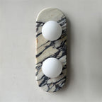 Clérachic marble wall light unlit on a plain grey wall, both opal glass globes shown clearly against the veining.