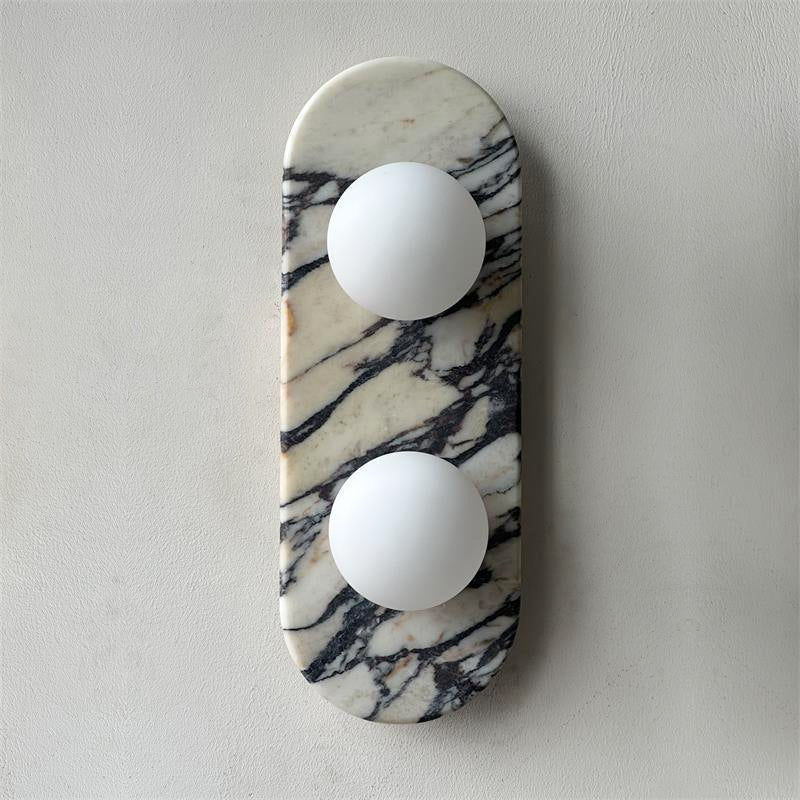 Clérachic marble wall light unlit on a plain grey wall, both opal glass globes shown clearly against the veining.