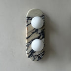 Clérachic marble wall light unlit, photographed close-in on a grey wall with the marble veining sharply visible.