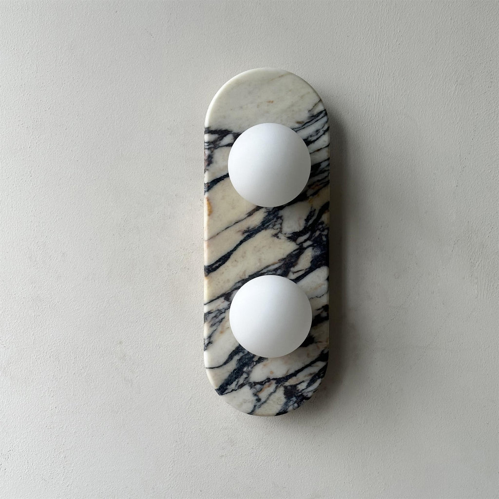Clérachic marble wall light unlit, centred on a plain grey wall with matte plaster texture visible around it.