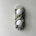 Clérachic marble wall light unlit, centred on a plain grey wall with matte plaster texture visible around it.