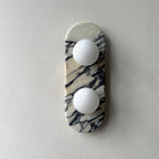 Clérachic marble wall light unlit, centred on a plain grey wall with matte plaster texture visible around it.