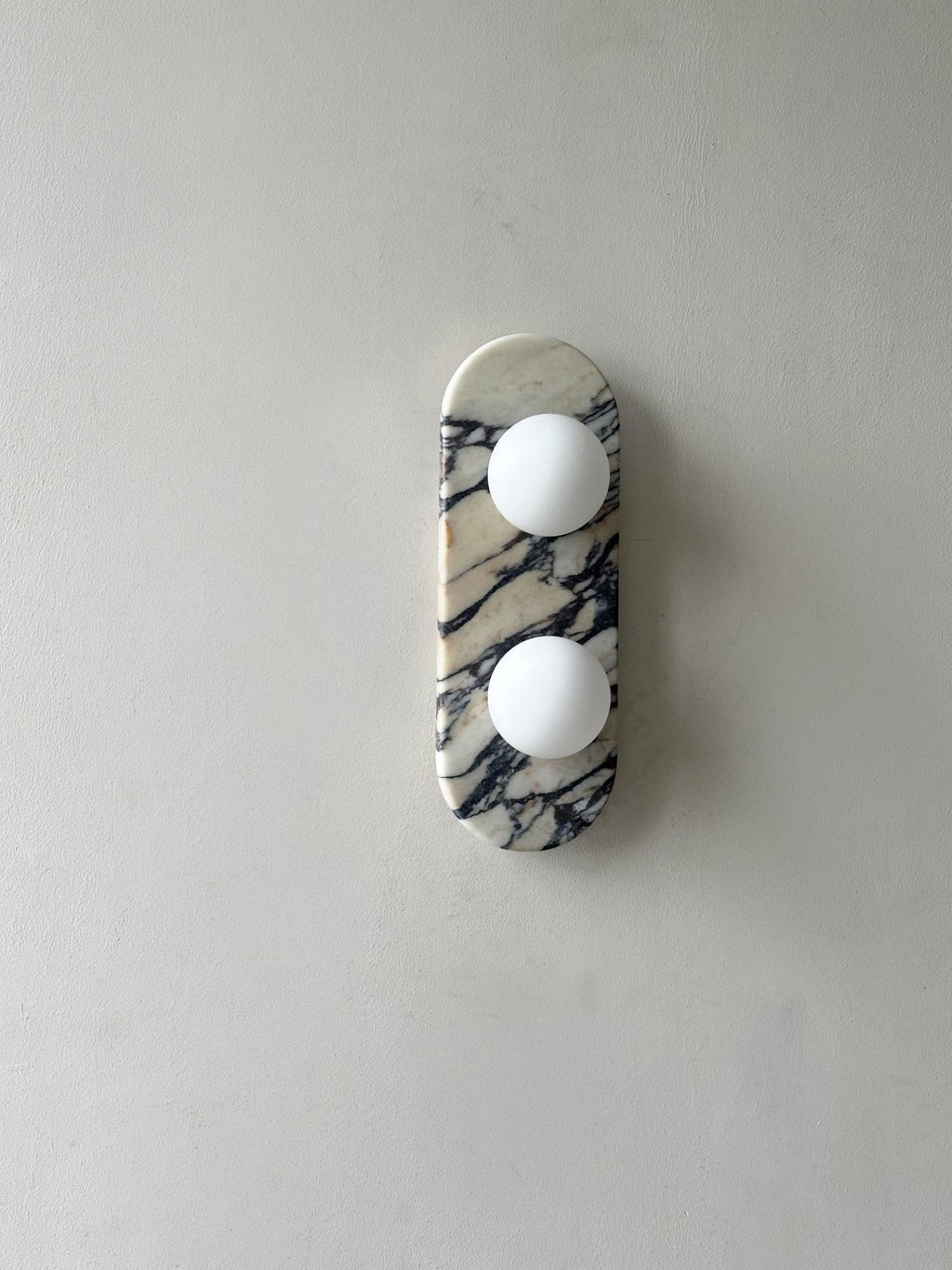 Clérachic marble wall light unlit, shown small and high on a plain grey wall with a wide margin of empty space.