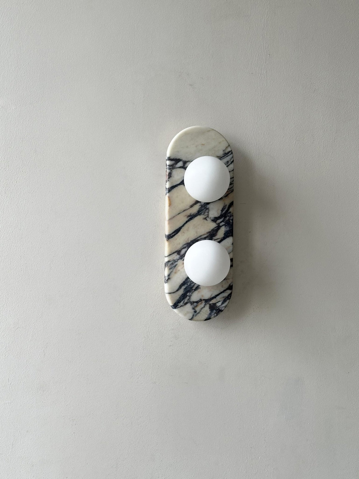 Clérachic marble wall light unlit, shown small and high on a plain grey wall with a wide margin of empty space.