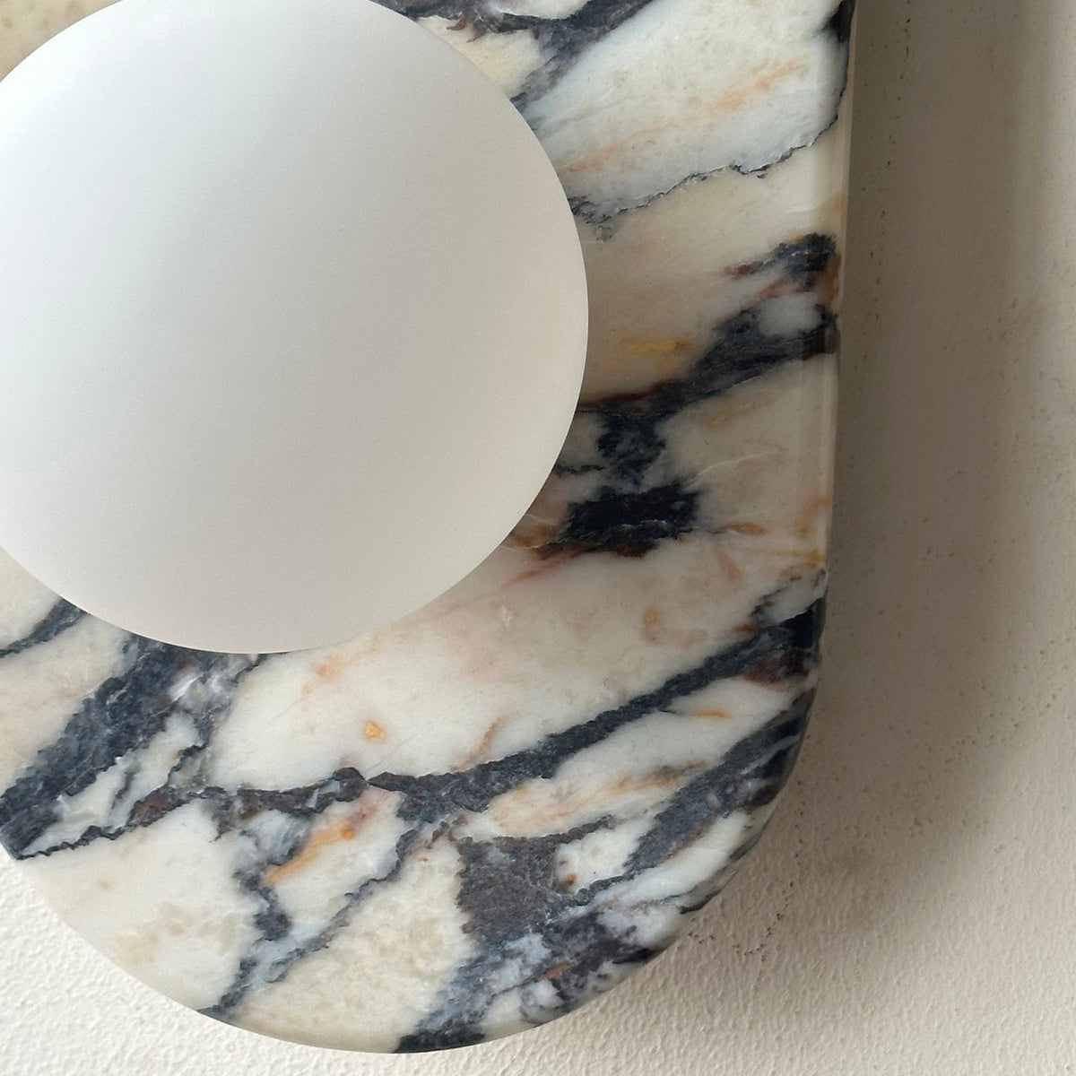 Clérachic marble wall light in close-up, showing the upper opal globe set into the veined marble plate.