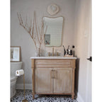 Beside a mirror in a bright bathroom, a Clérachic wall light sits above a marble-top vanity with a vase of dry branches.