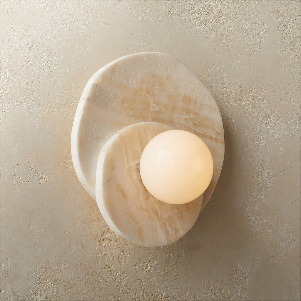 Mounted on a textured plaster wall, the Clérachic stone wall light shows its layered alabaster discs and glass globe up close.