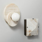 The alabaster Clérachic wall light hangs beside a matching stone switch plate, both mounted on a plain painted wall.