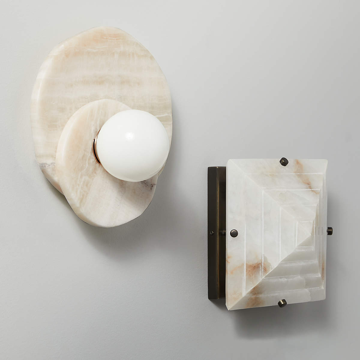 The alabaster Clérachic wall light hangs beside a matching stone switch plate, both mounted on a plain painted wall.