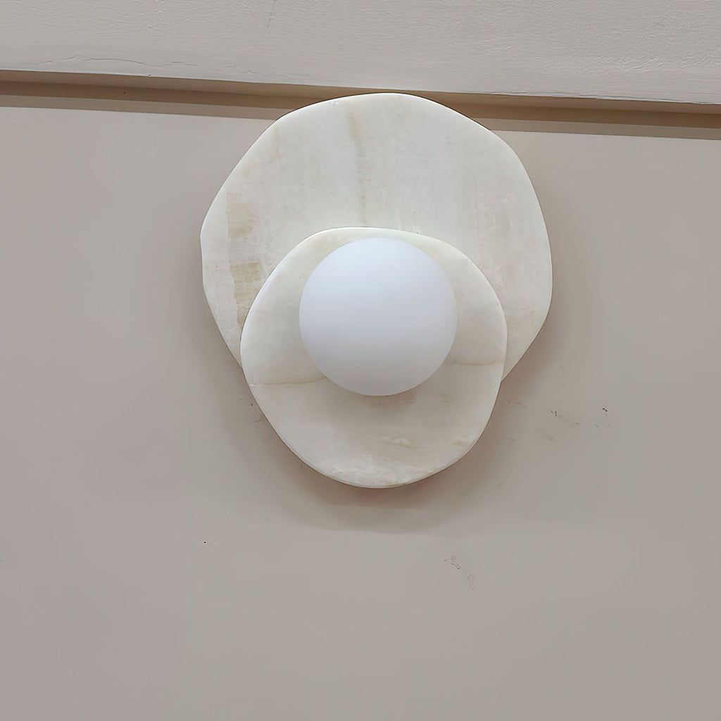 Seen at a slight angle on a plain wall, the alabaster Clérachic wall light's two discs overlap around its lit glass globe.