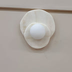 Seen at a slight angle on a plain wall, the alabaster Clérachic wall light's two discs overlap around its lit glass globe.