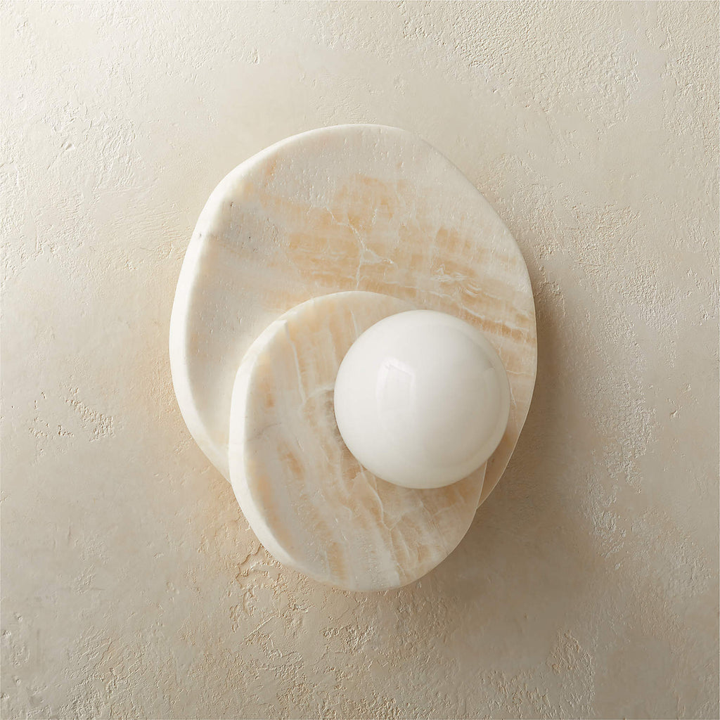 Front-on against a rustic beige wall, the alabaster Clérachic wall light's stacked discs catch warm natural daylight.