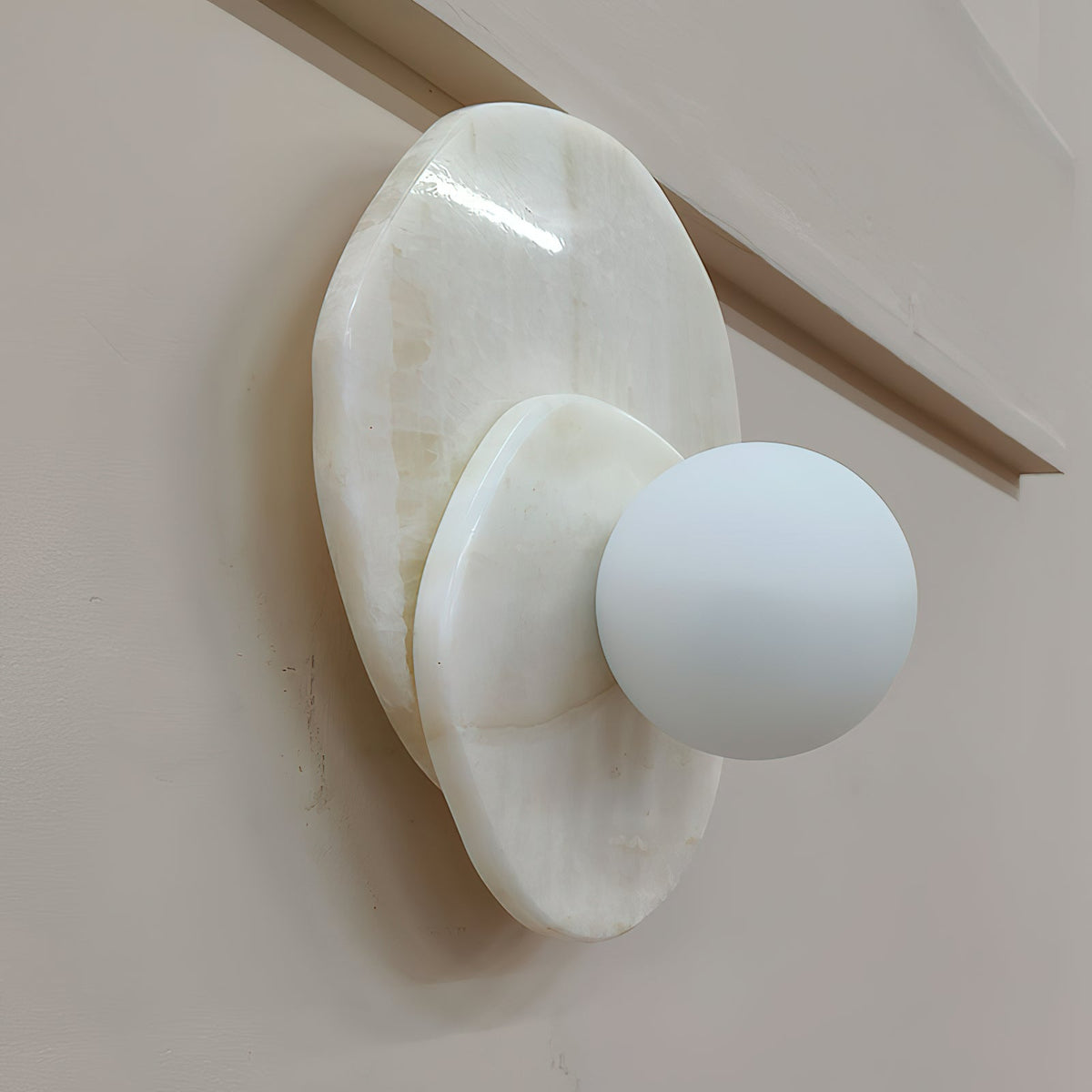 Beside a wooden stair handrail, the Clérachic wall light's pale stone discs hold a softly lit globe at head height.