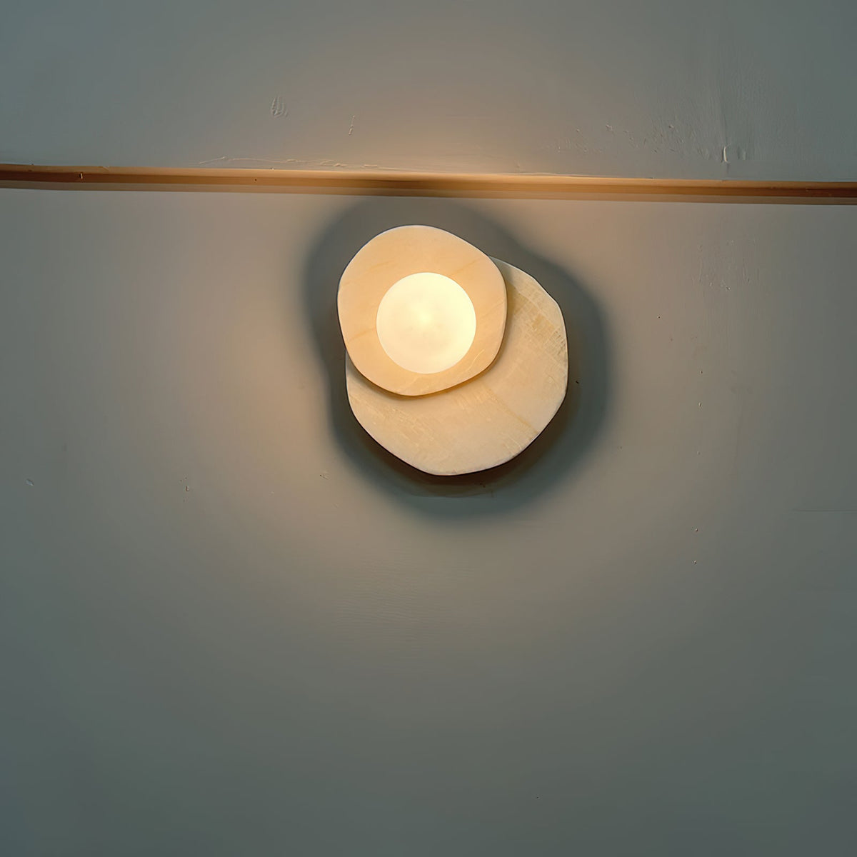 Glowing against a dark teal wall beneath a brass rail, this Clérachic wall light's globe stands out in a moody night shot.