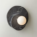 In dark marble with white veining, this Clérachic wall light glows against a plain wall, its stone grain clearly visible.