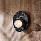 In black marble with pale veining, this Clérachic wall light sits on a wood-panelled wall, its globe lit against the grain.