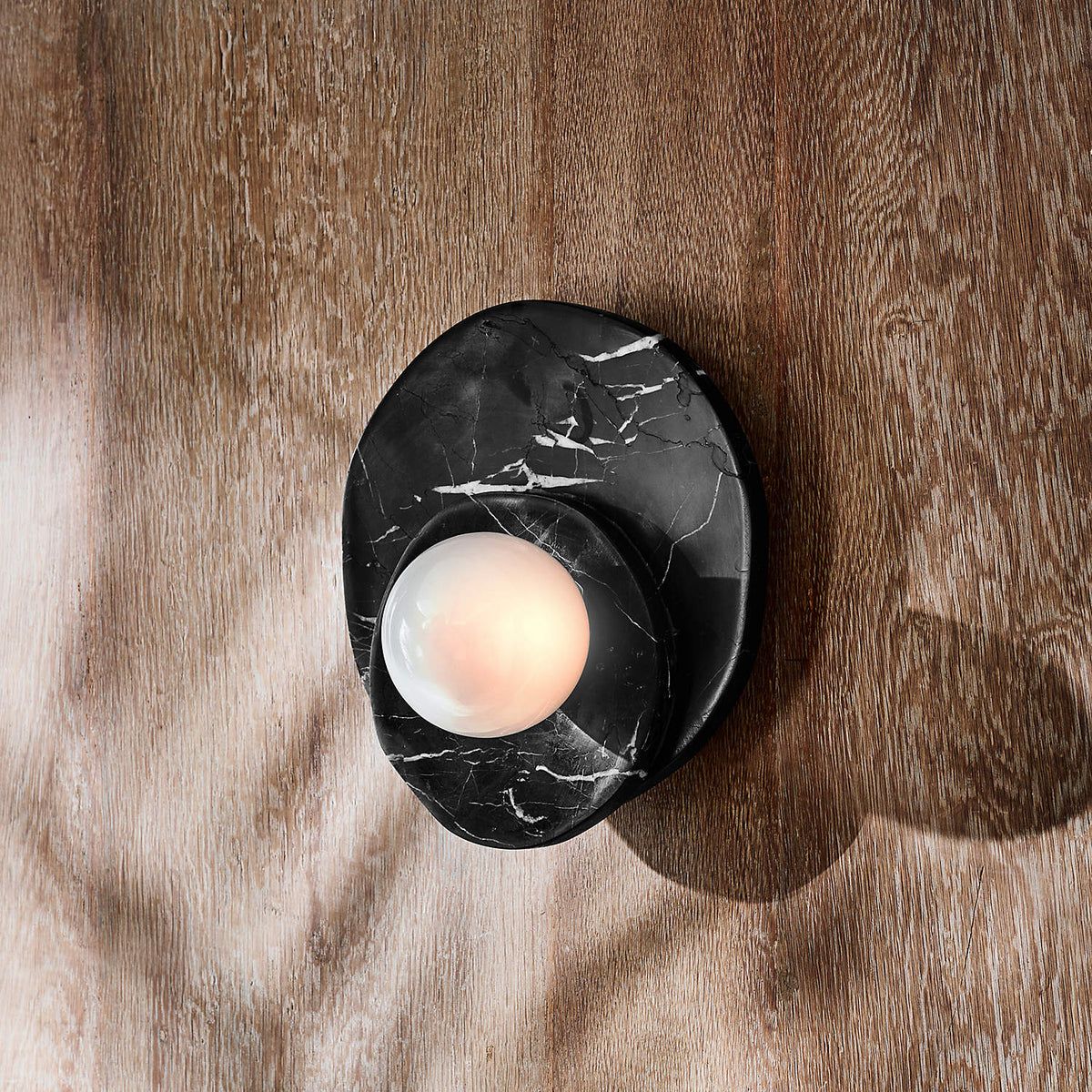 In black marble with pale veining, this Clérachic wall light sits on a wood-panelled wall, its globe lit against the grain.