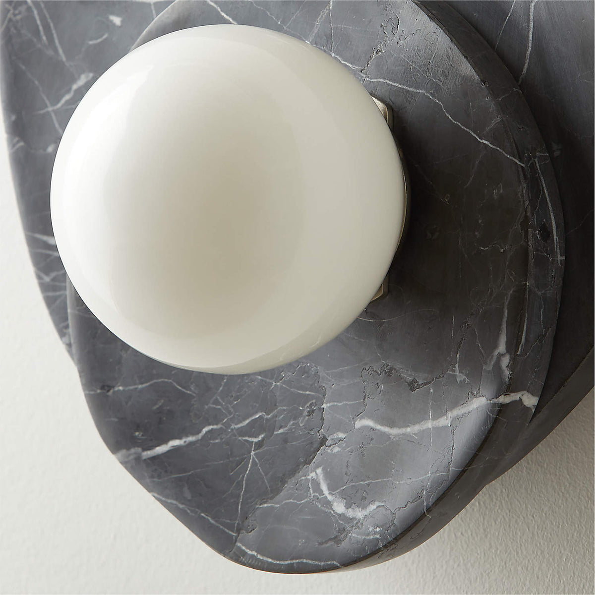 An extreme close-up shows the Clérachic wall light's black marble veining wrapped around a glass globe on a curved surface.