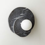 In black marble on a plain white wall, this Clérachic wall light is shown straight-on with its glass globe centred low.