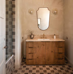 Flanking a bathroom mirror above a wood vanity, two Clérachic wall lights sit on a plaster wall over checked tile flooring.