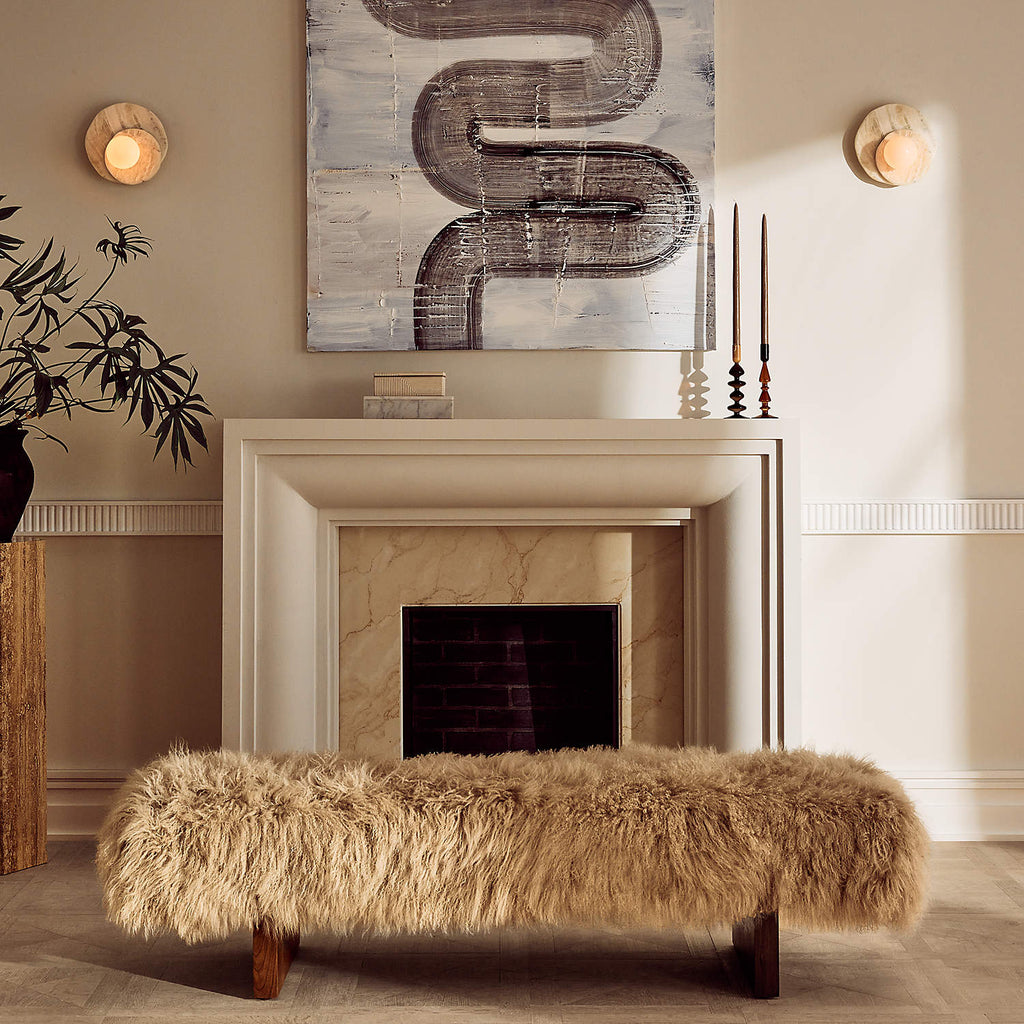 Either side of a stone fireplace, Clérachic wall lights glow softly above a cream mantel and a shaggy fur bench.