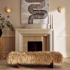 Either side of a stone fireplace, Clérachic wall lights glow softly above a cream mantel and a shaggy fur bench.