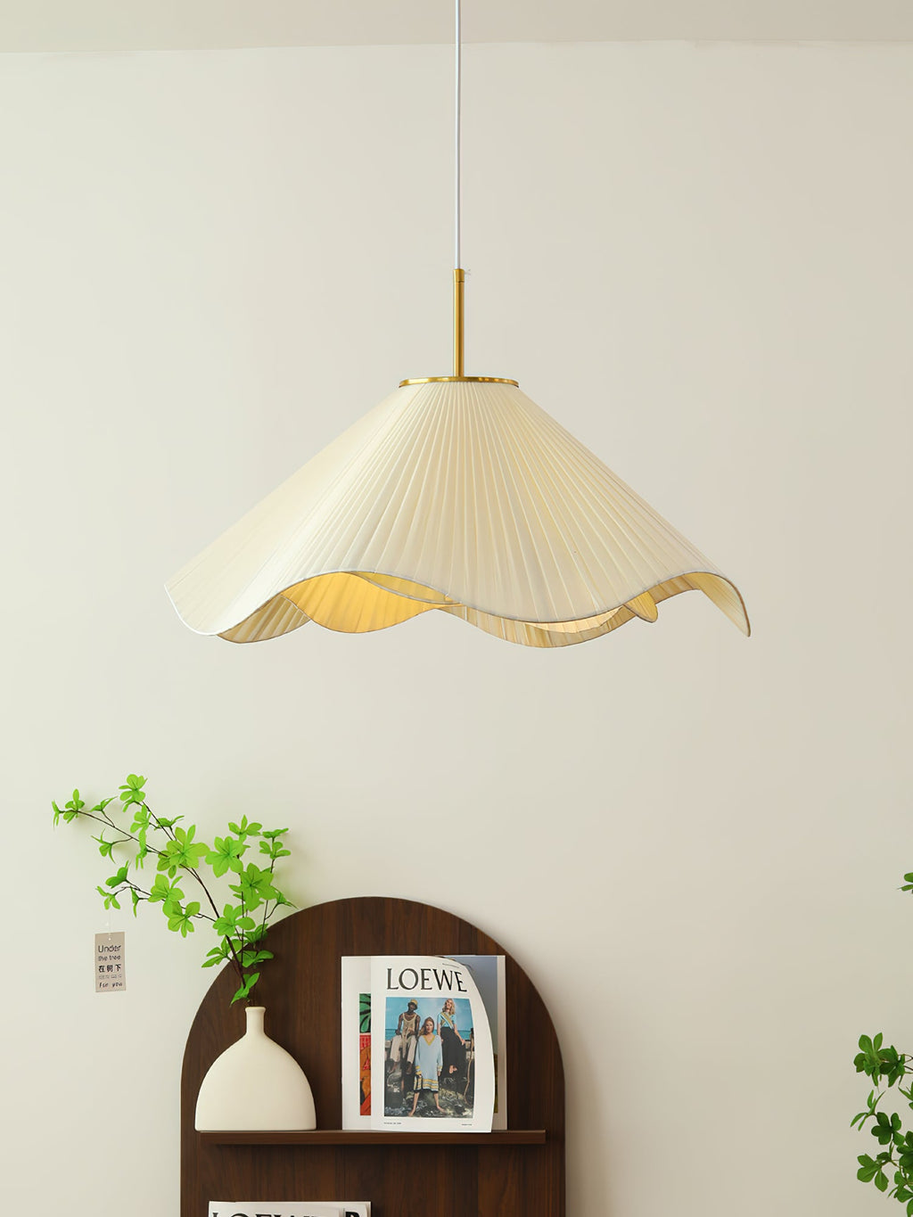 A trailing green vine climbs beside this beige Clérachic pendant light above a dark wood console.