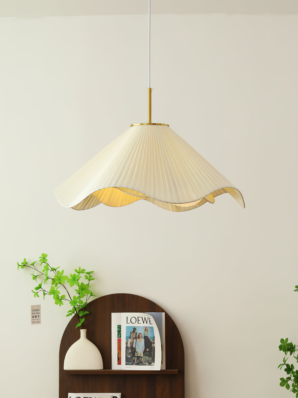 A trailing green vine climbs beside this beige Clérachic pendant light above a dark wood console.