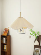 Beside a wooden bookshelf stacked with books, this beige Clérachic pendant light glows above a small vase.