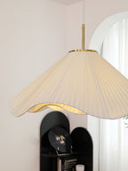 Above a black cabinet styled with ceramic pieces and a magazine, this beige Clérachic pendant light hangs lit.