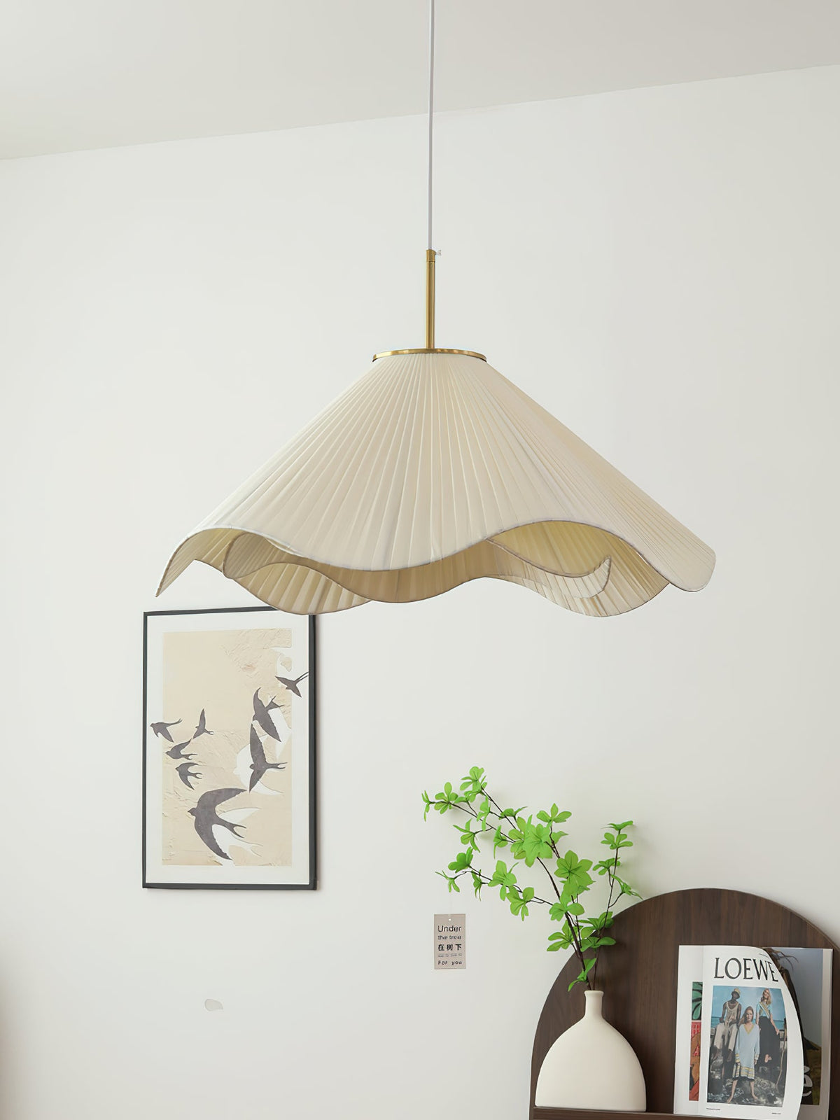 This beige Clérachic pendant light glows beside a framed bird print on a plain cream wall.