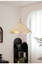 Near a black shelving unit topped with a trailing plant, this beige Clérachic pendant light hangs softly lit.
