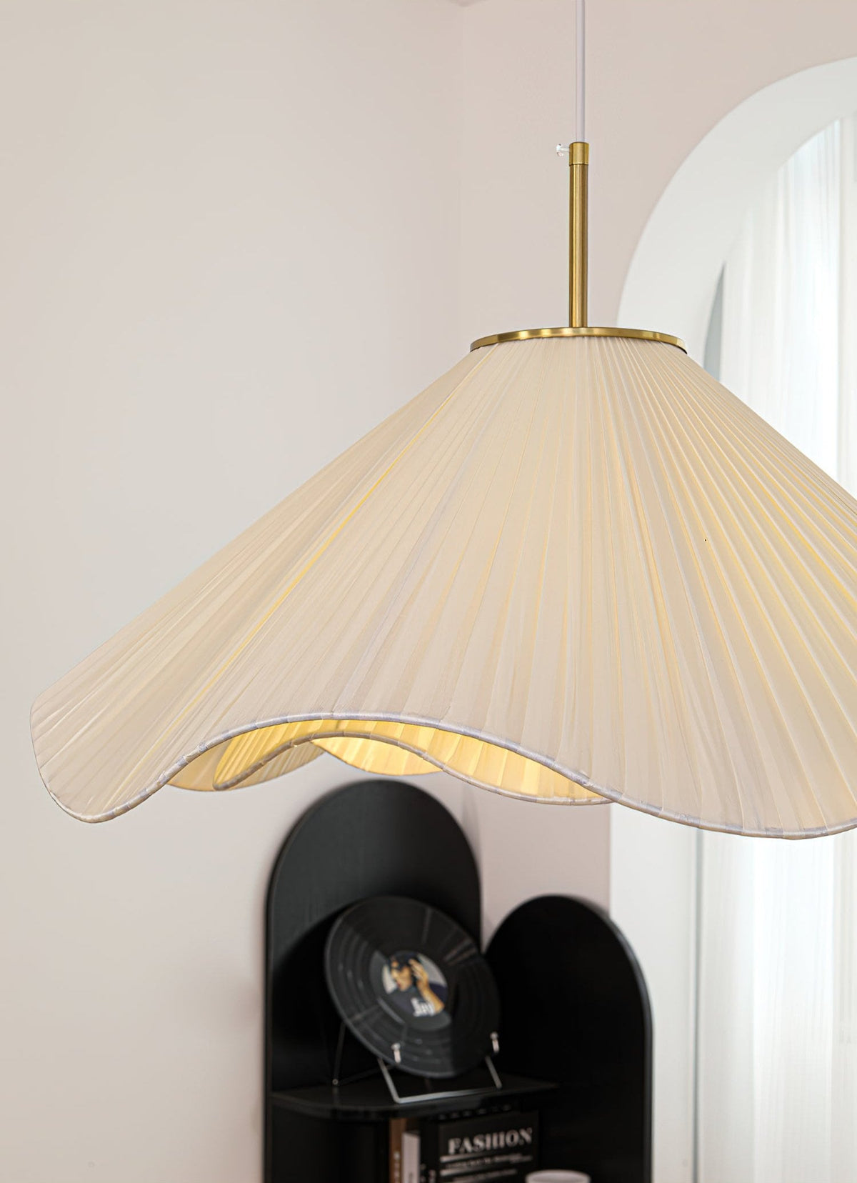 Near an arched doorway, this beige Clérachic pendant light glows beside a black shelving unit.