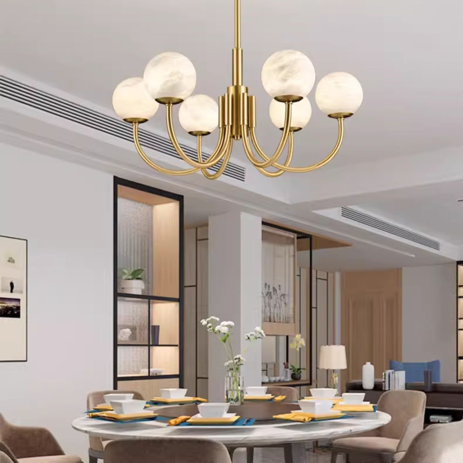 Clérachic lit above a round marble dining table laid for a meal in an open-plan apartment