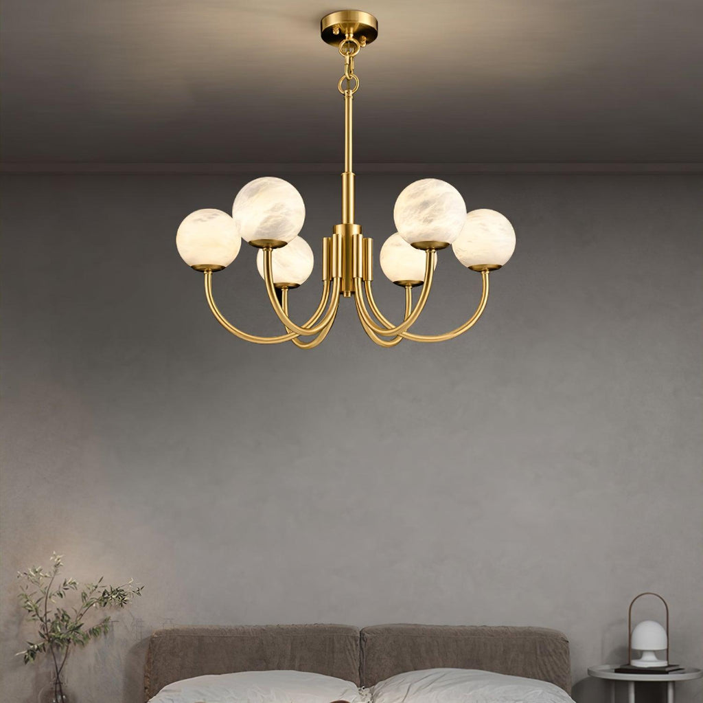 The Clérachic chandelier lit over a bed against a plain grey plaster wall, nightstand lamp glowing