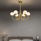 The Clérachic chandelier lit over a bed against a plain grey plaster wall, nightstand lamp glowing