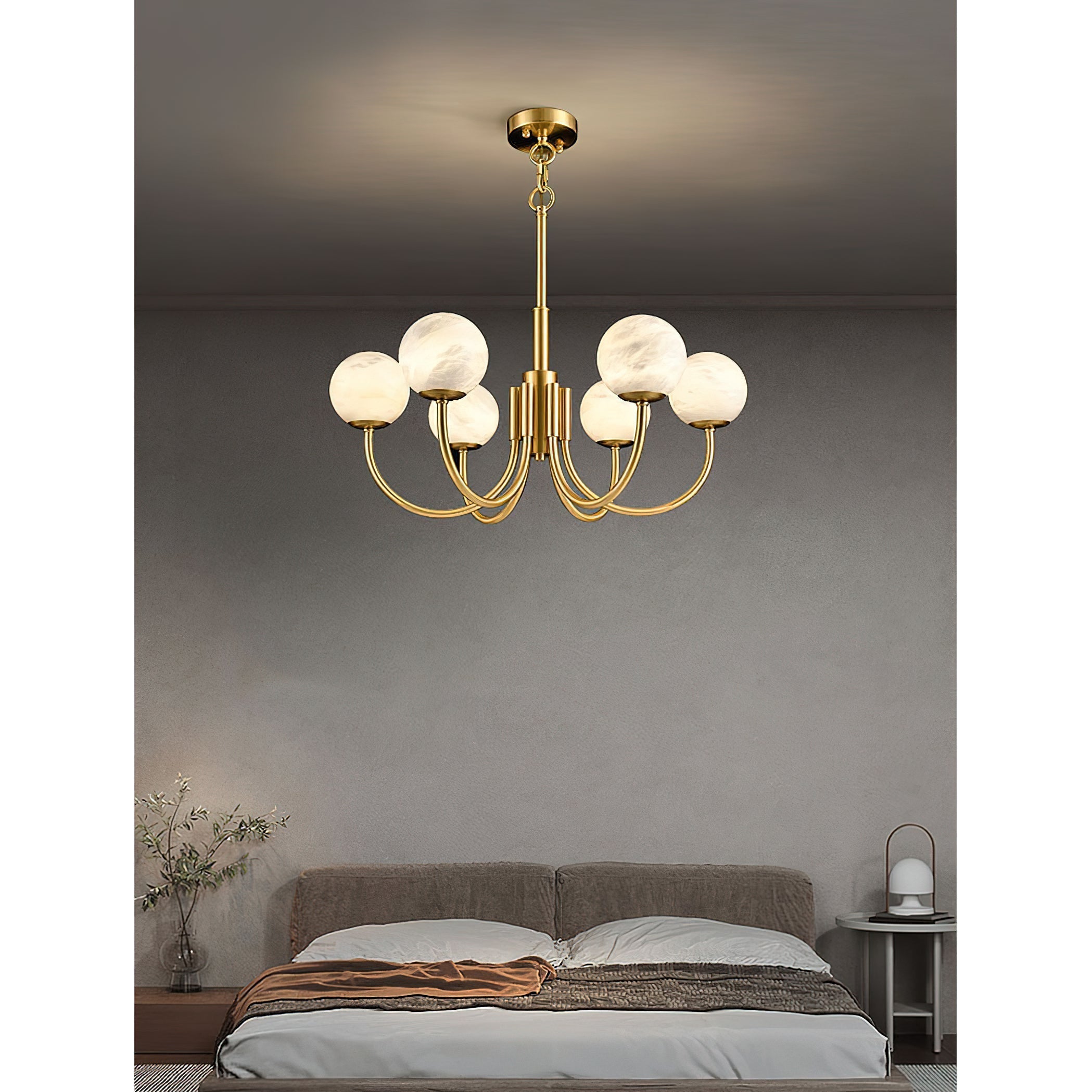 The Clérachic chandelier lit above a low bed dressed in grey linen, beside an olive branch in a vase