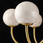 Clérachic close-up of three alabaster globes seated on brass arms, showing the stone's cloudy veining